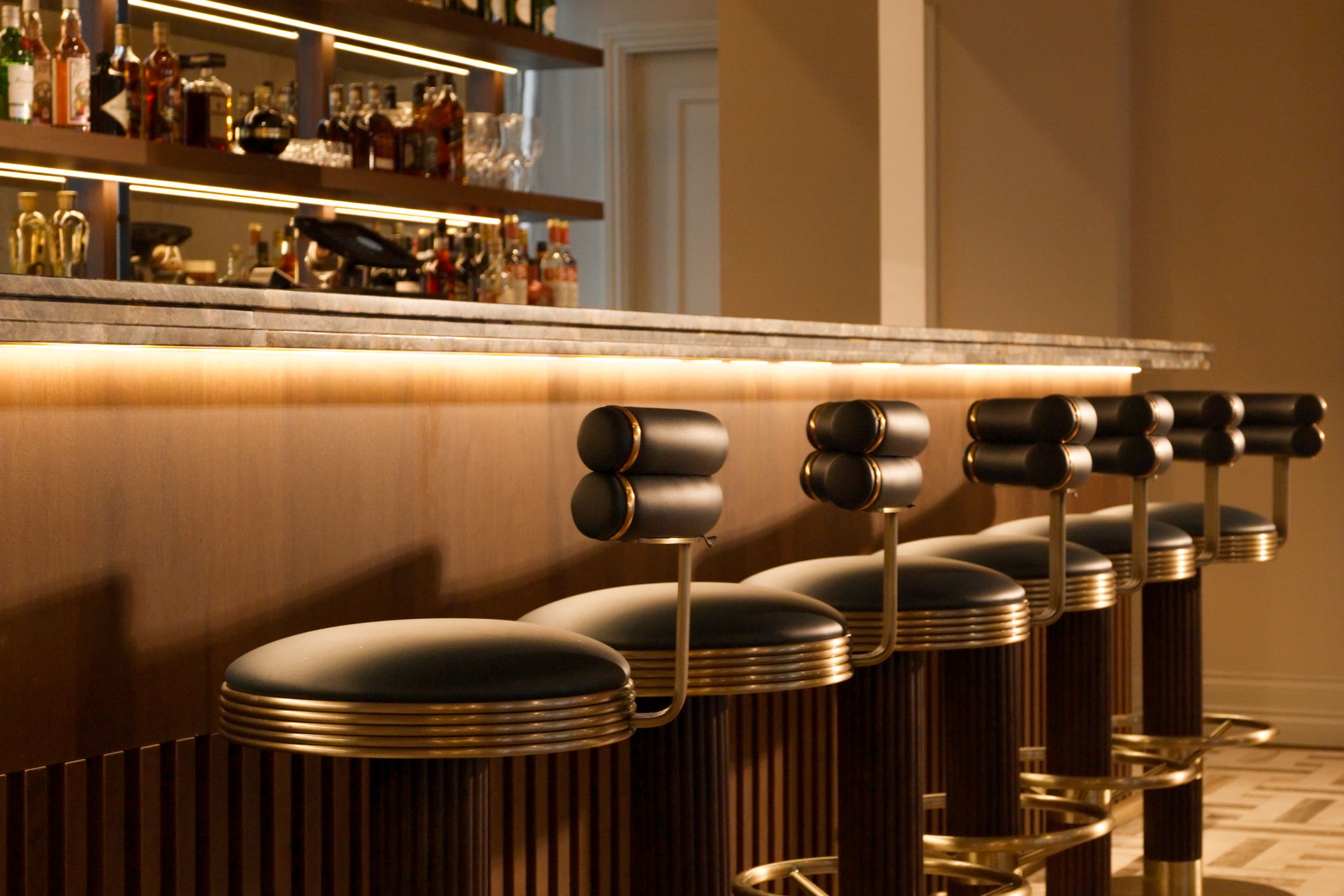 Hotel bar with leather and brass stools beneath a marble counter lit from below