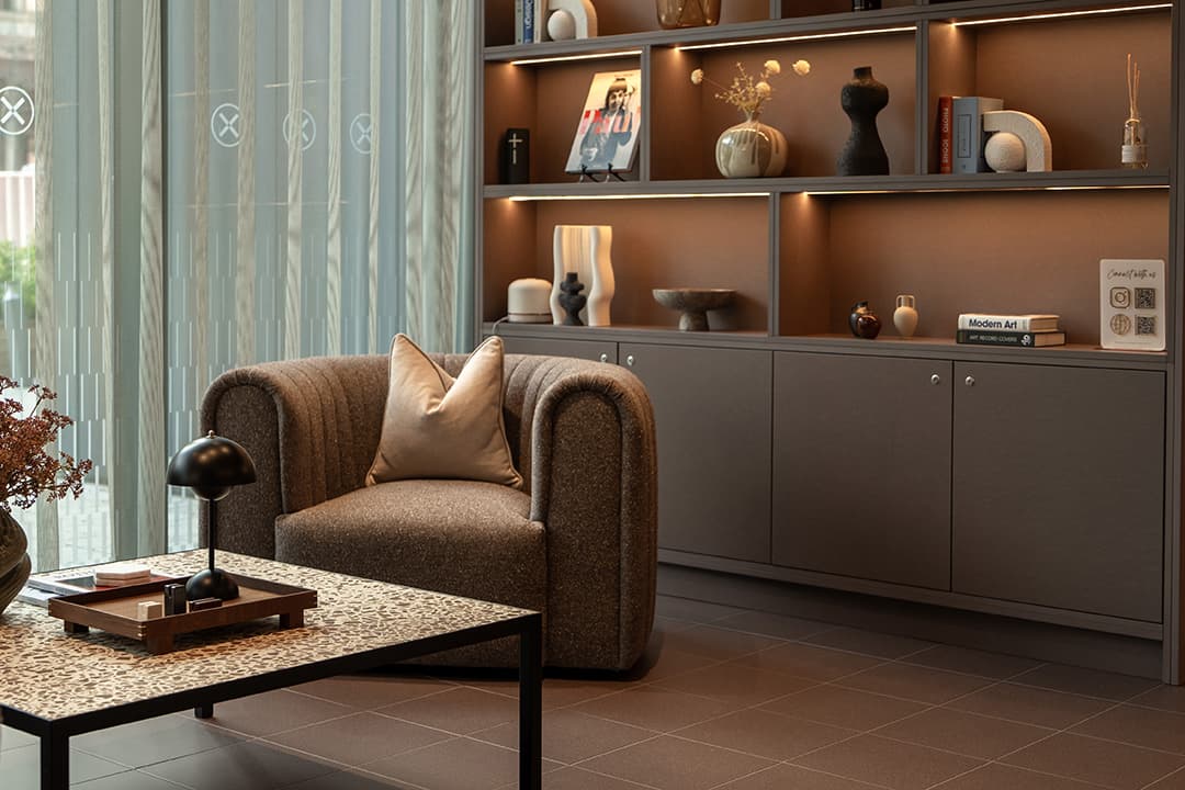 Armchair beside a backlit display shelf styled with books, vases and ceramics