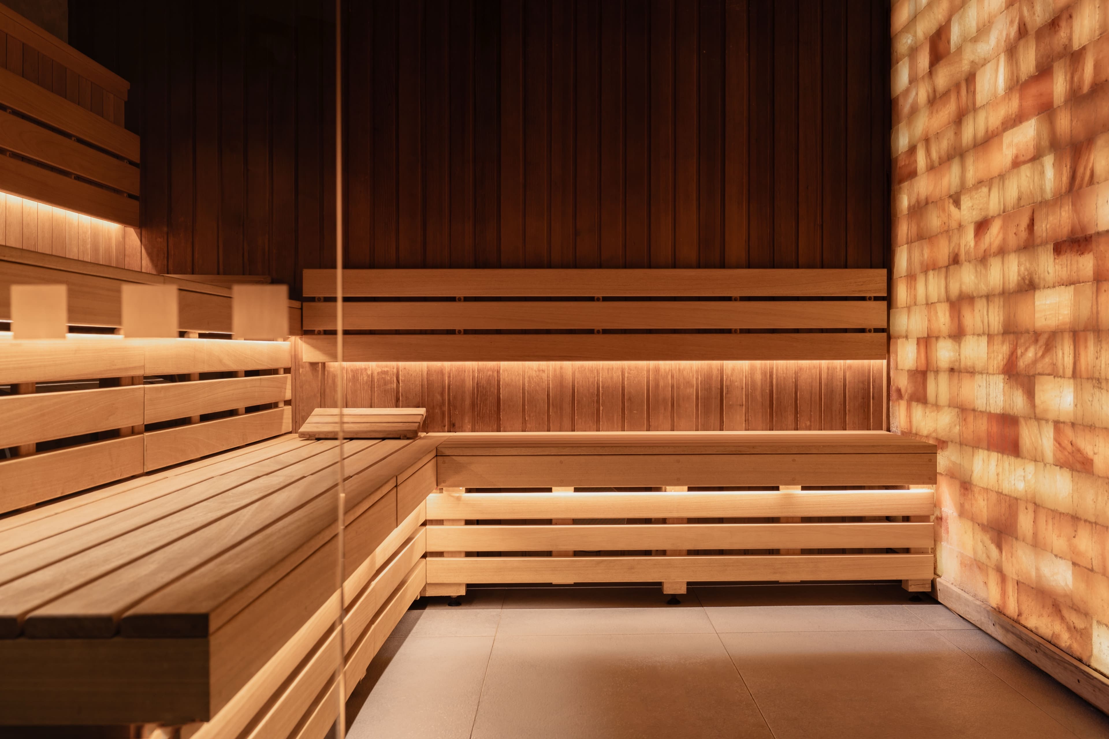 Sauna with slatted timber benches, warm strip lighting and a glowing Himalayan salt brick wall
